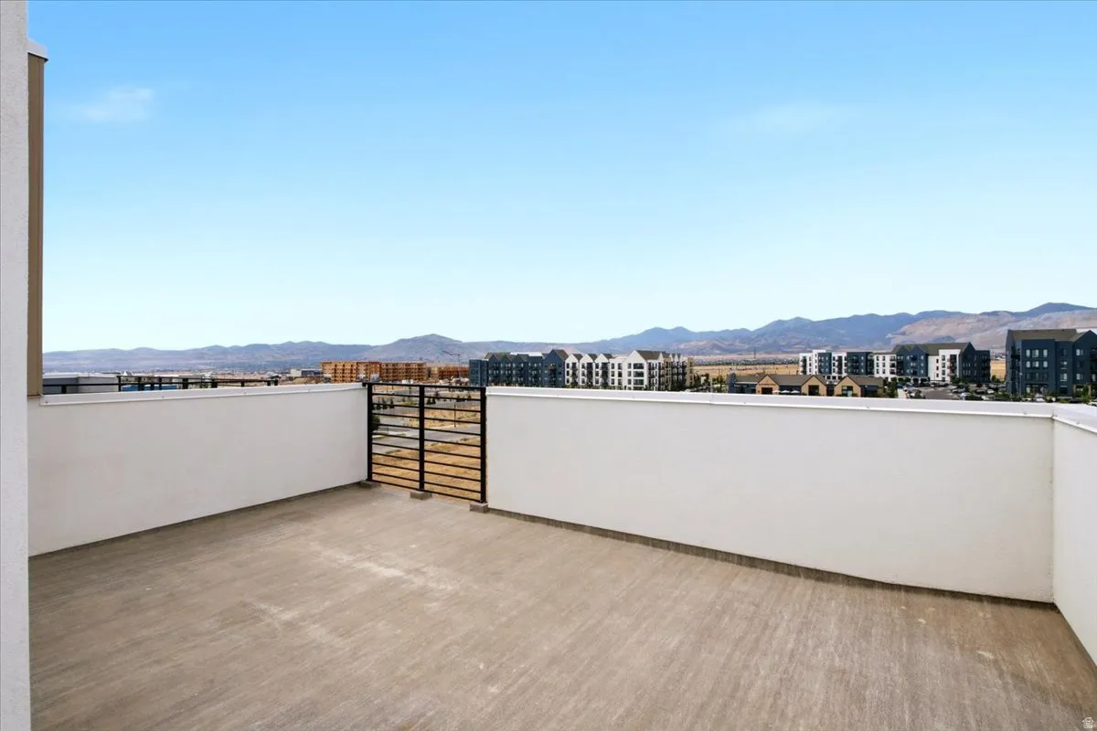 Spacious rooftop terrace featuring concrete flooring, a black metal gate, and white parapet walls