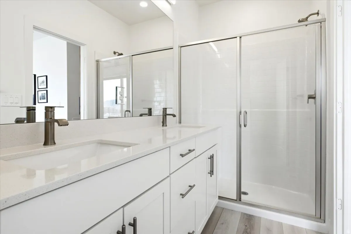 Dual vanity with white cabinetry and integrated sinks featuring bronze-finish faucets, complemented by a glass-enclosed shower with a textured wall