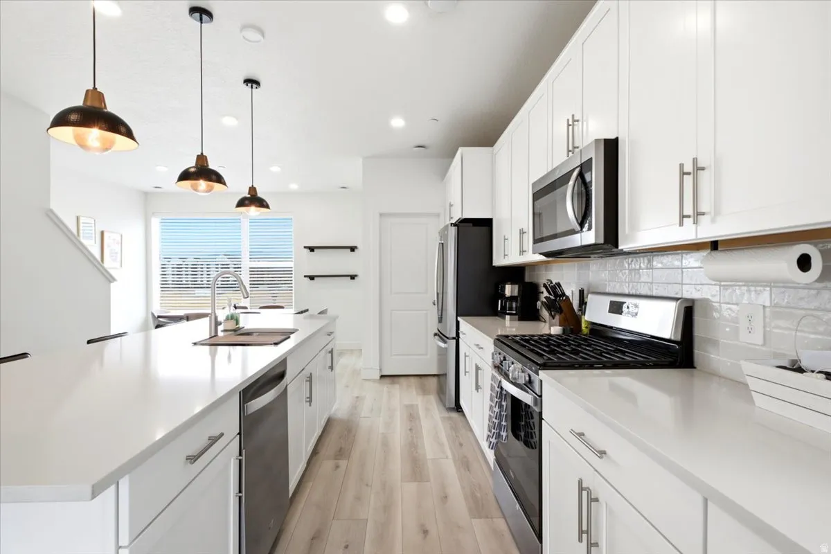 Kitchen featuring an expansive island with a stainless steel sink, white cabinetry with brushed nickel hardware, light wood-finish flooring, stainless steel appliances, and subway tile backsplash
