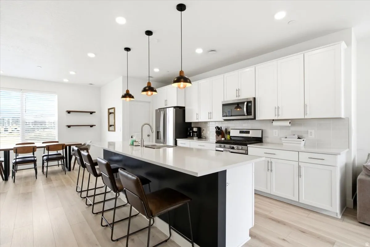 Modern kitchen featuring white cabinetry, stainless steel appliances, a spacious island with counter seating, light wood-finish flooring, and recessed lighting