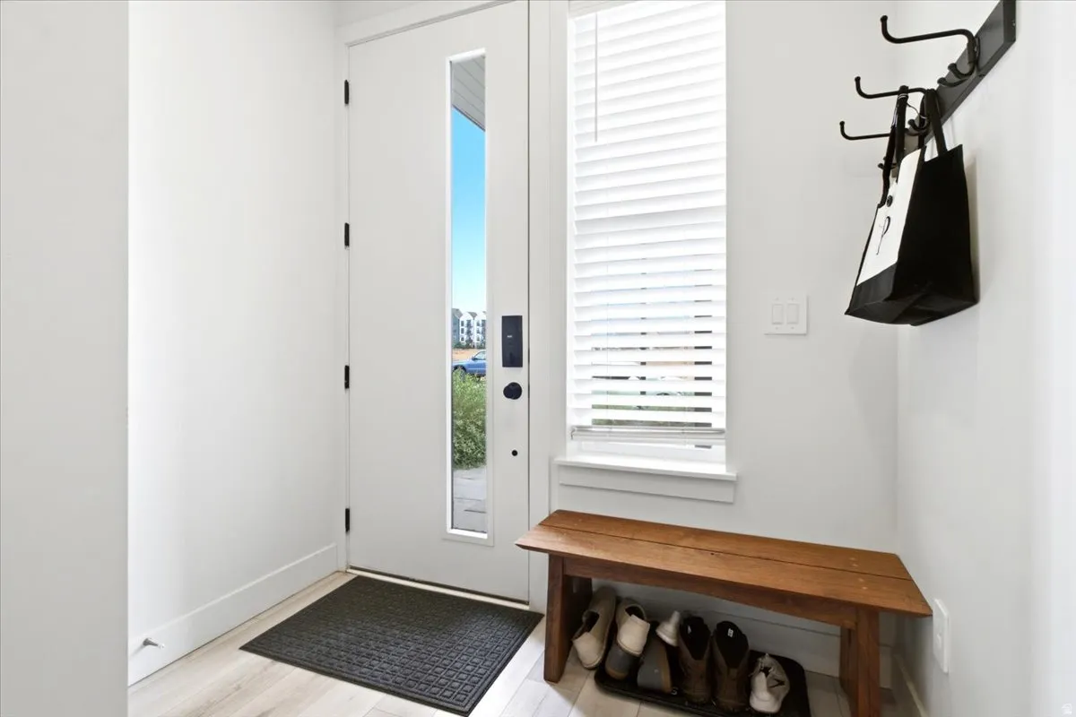 Entryway featuring a white door with a vertical glass panel, wood-finish flooring, a window with blinds, and a built-in coat rack
