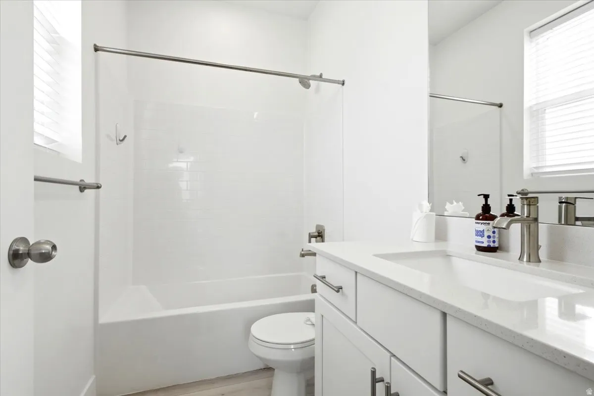 Bathroom featuring a vanity with an integrated sink and light-toned countertop, a rectangular mirror, a window with blinds, and a tub with a shower and subway tile surround