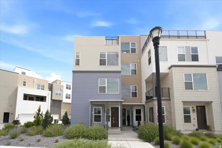 Modern multi-level townhome featuring multiple balconies, a rooftop deck with metal railing, and a blend of siding and brick exterior finishes