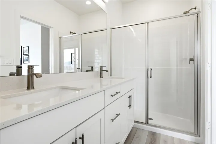 Dual vanity with white cabinetry and integrated sinks featuring bronze-finish faucets, complemented by a glass-enclosed shower with a textured wall