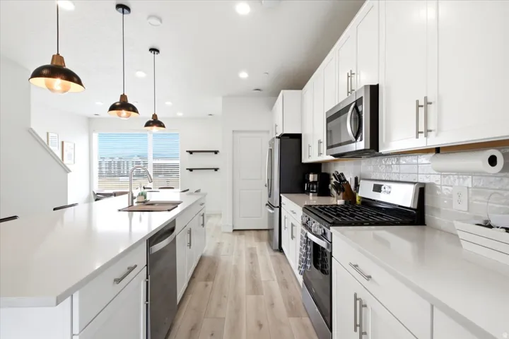 Kitchen featuring an expansive island with a stainless steel sink, white cabinetry with brushed nickel hardware, light wood-finish flooring, stainless steel appliances, and subway tile backsplash