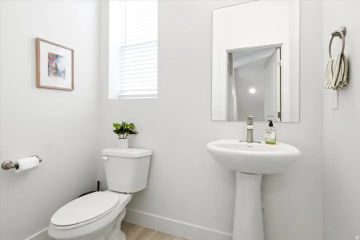 Powder room featuring a pedestal sink with a single-handle faucet, a wall-mounted mirror, a standard toilet, and wood-finish flooring