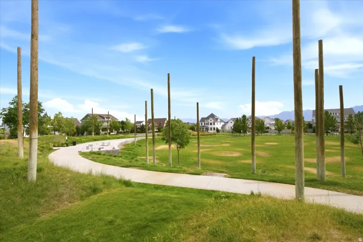 Expansive green space featuring a paved walking path, sculptural wood elements, and an amphitheater-style seating area