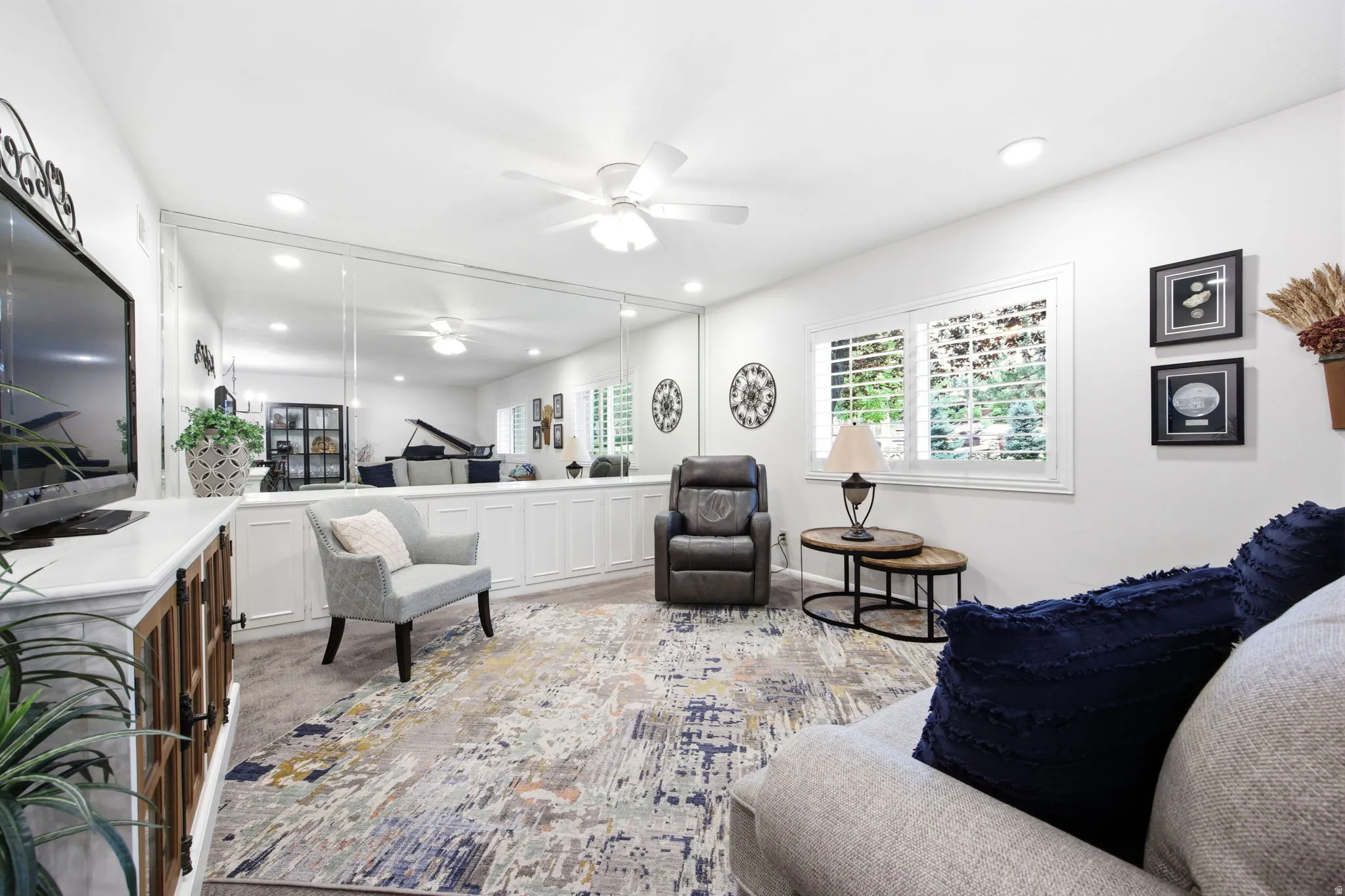 Spacious room featuring a full wall of mirrors above extensive built-in cabinetry, dual windows with plantation shutters, recessed lighting, and a ceiling fan