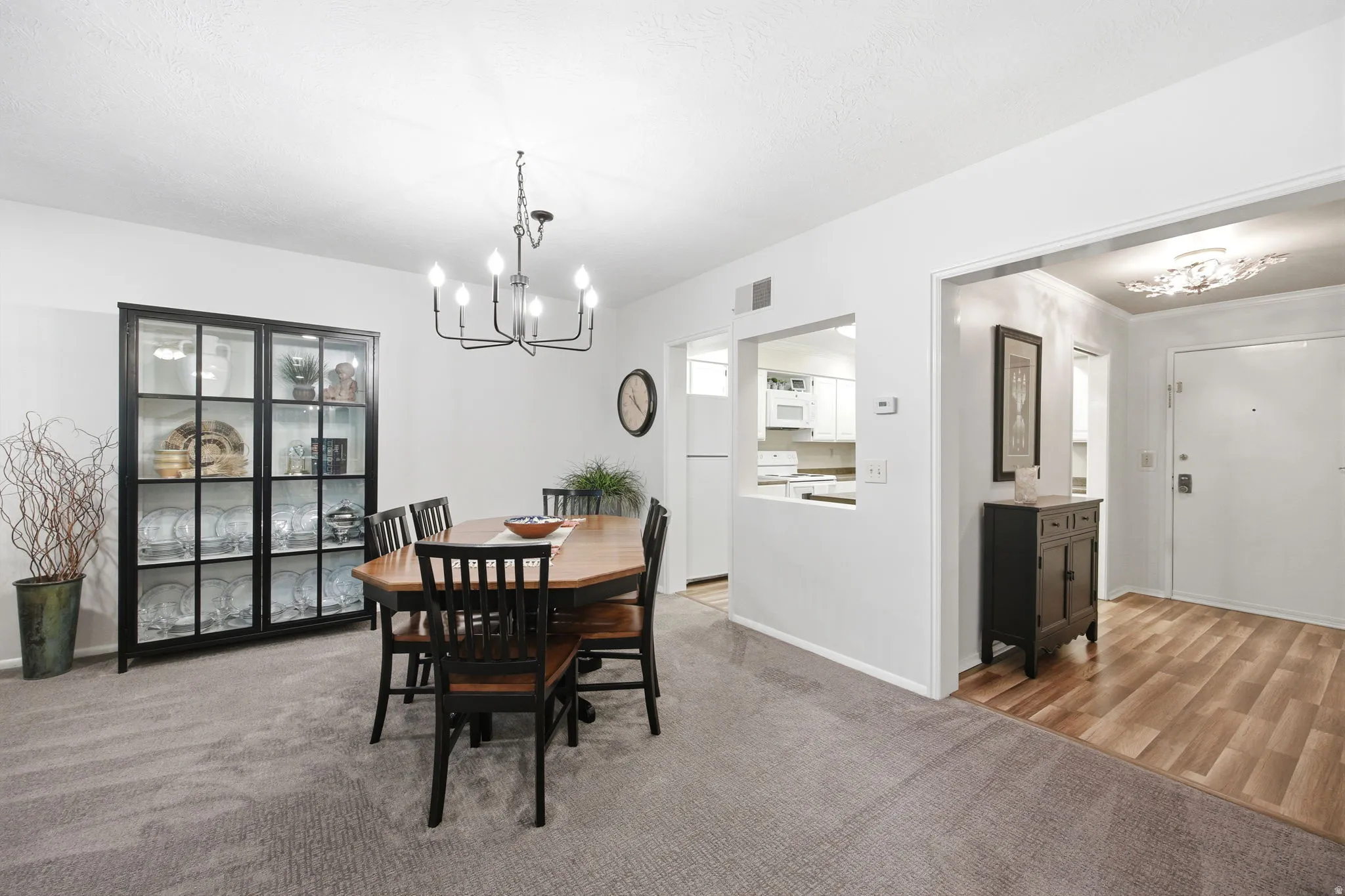 Carpeted dining area with a multi-arm chandelier, an open pass-through to the kitchen, and a wood-finish flooring entryway