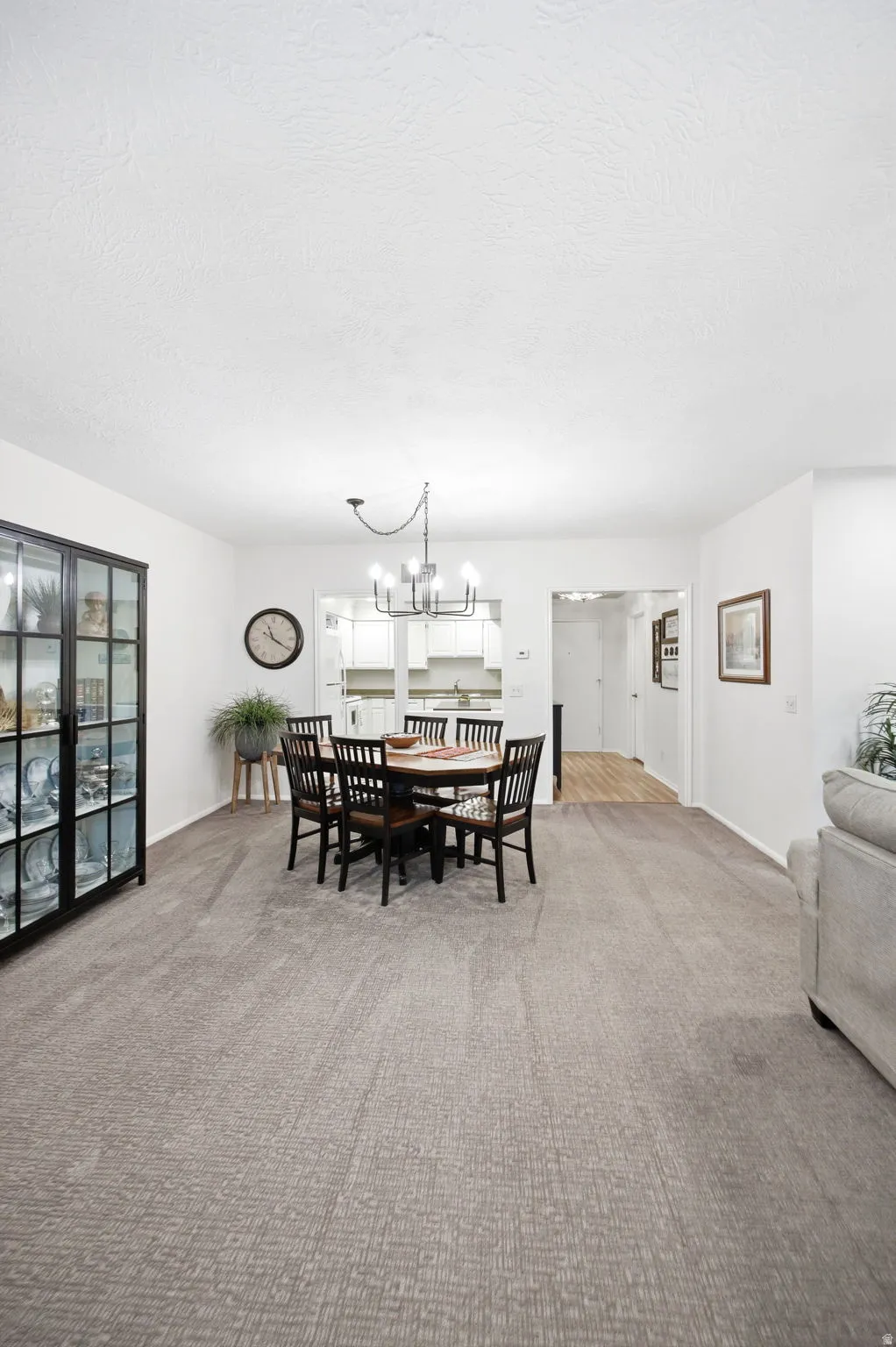 Open-concept dining area featuring a contemporary chandelier, textured carpet flooring, and white walls