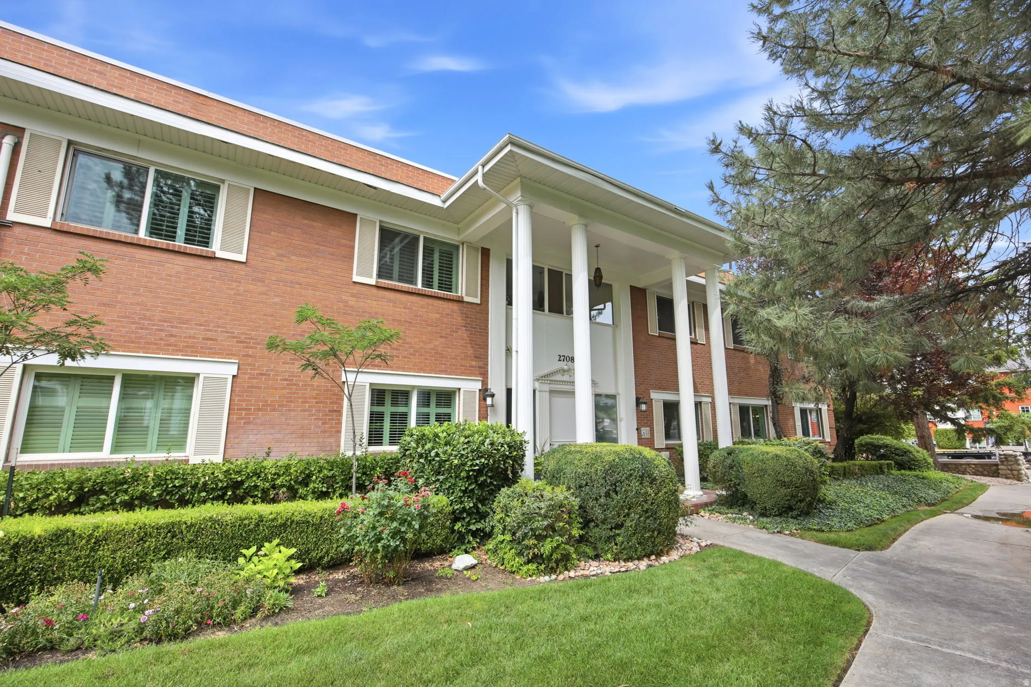 Brick exterior featuring white columns, a covered entry, and multiple windows with white shutters
