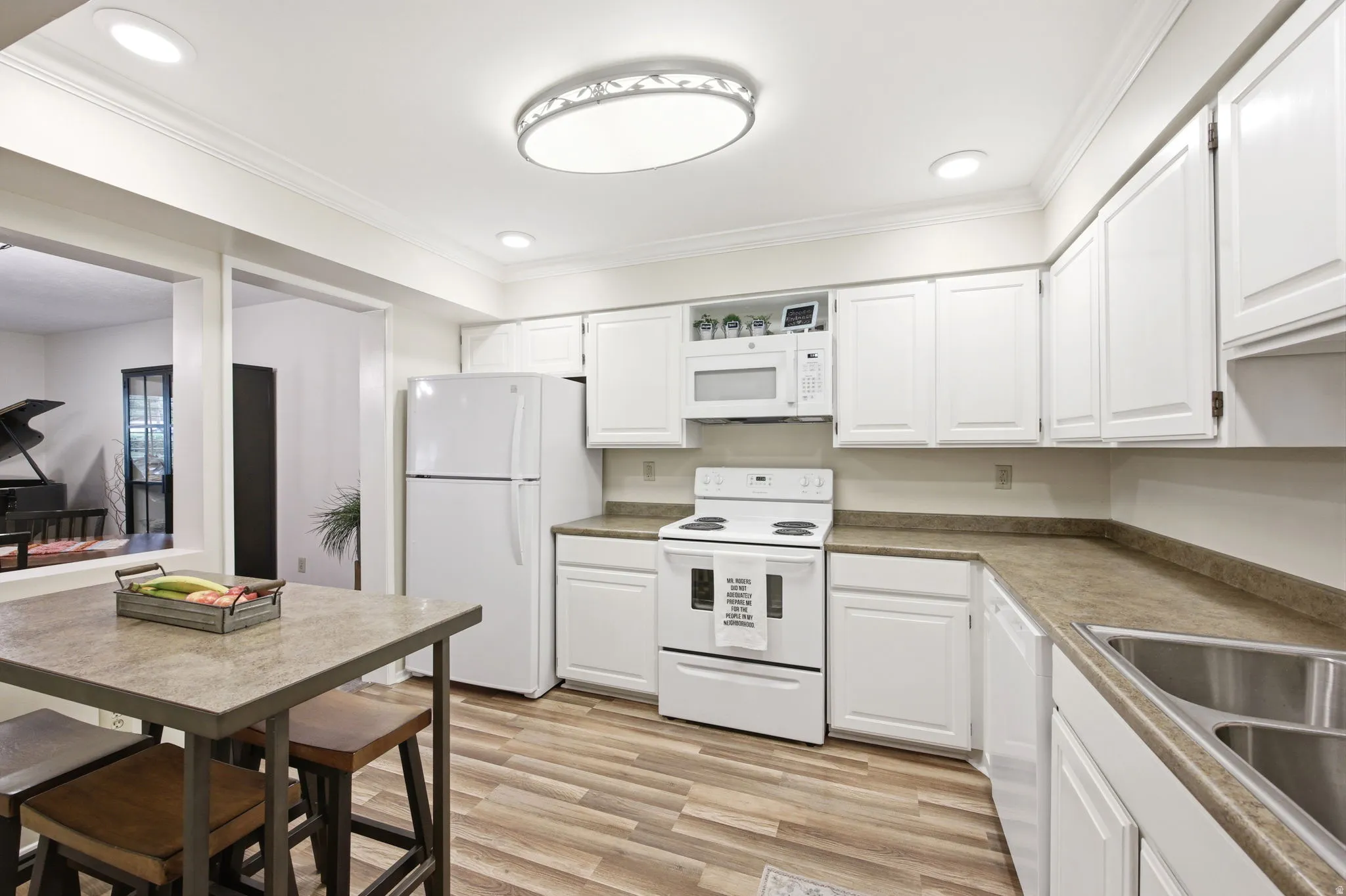 Kitchen featuring white cabinetry, light-toned countertops, a built-in microwave, a double basin stainless steel sink, and wood-finish flooring