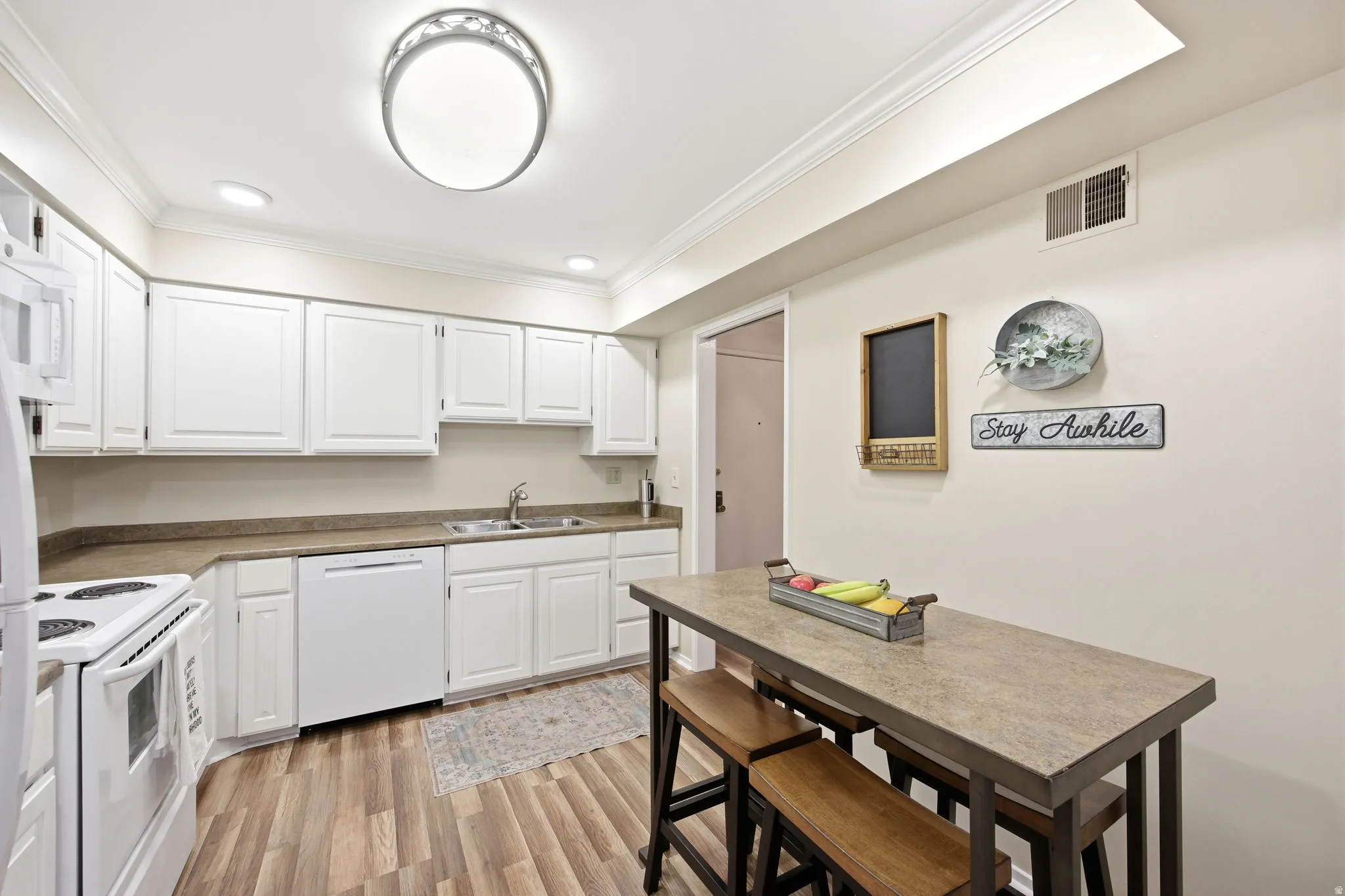 Kitchen featuring white cabinetry, light-toned countertops, wood-finish flooring, recessed lighting, and crown molding