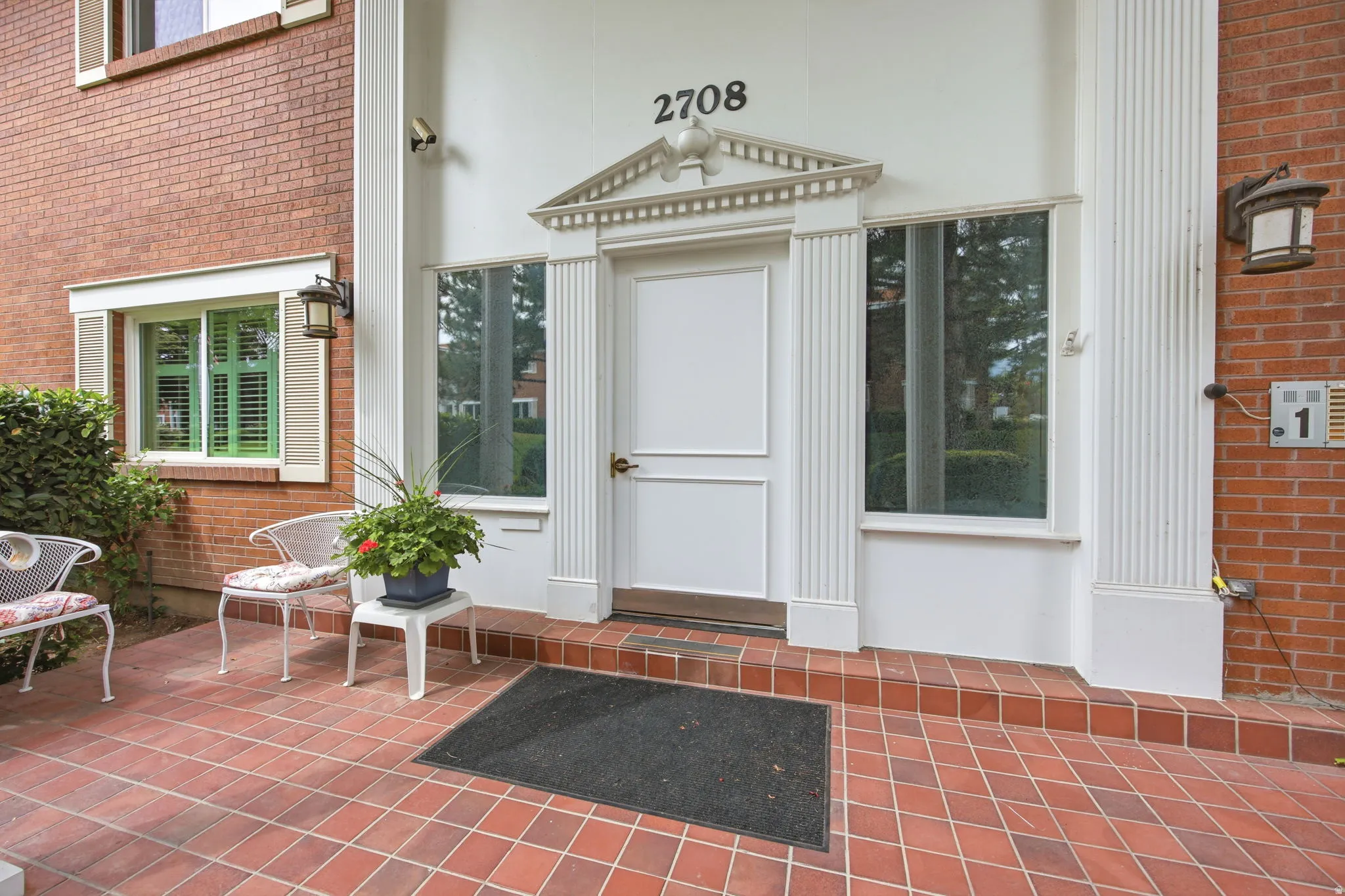 Entryway with a terracotta tile patio, brick facade, and a white architectural door surround