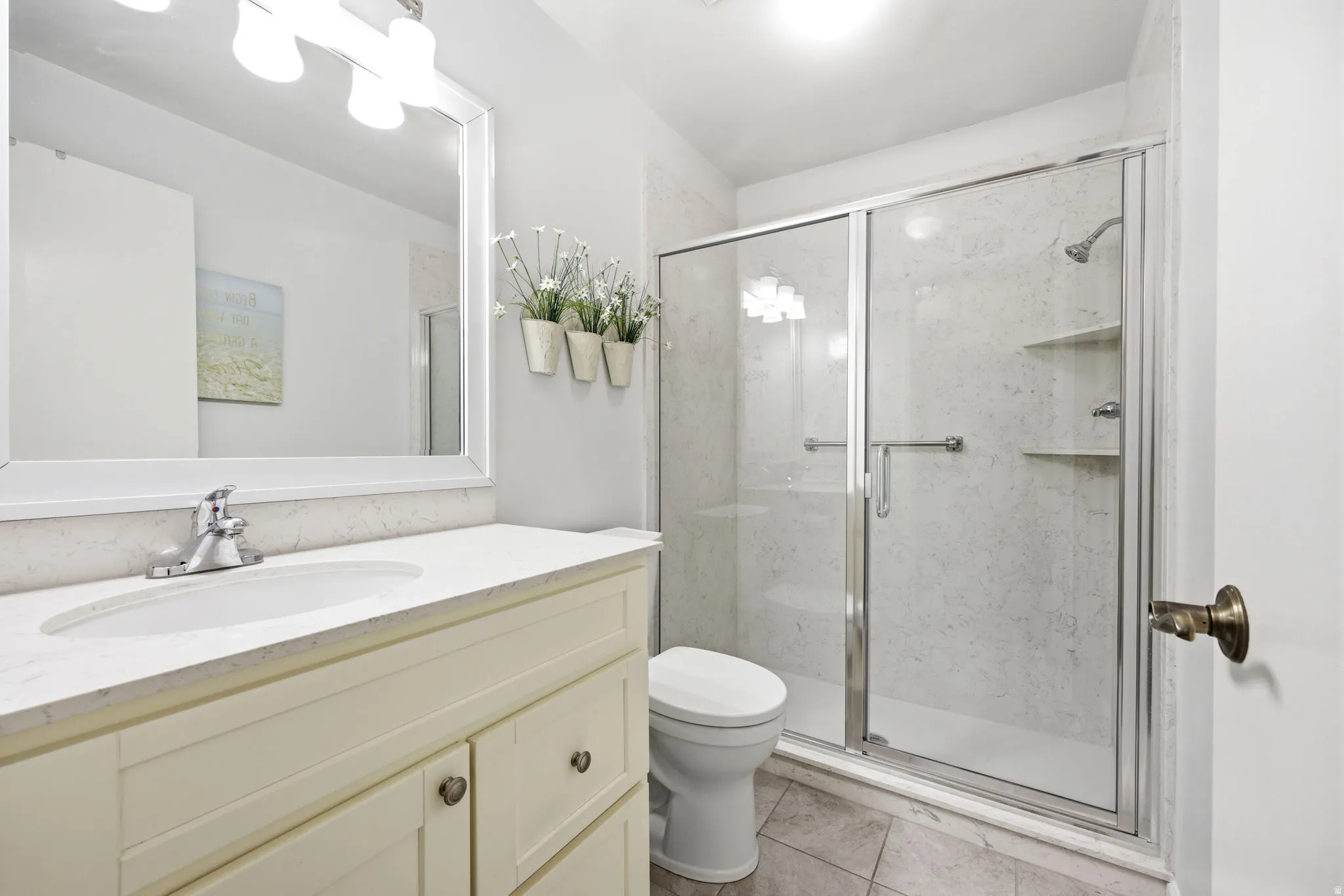 Bathroom featuring a light-toned vanity with an integrated sink and chrome faucet, a framed mirror, and a glass-enclosed shower with interior shelving