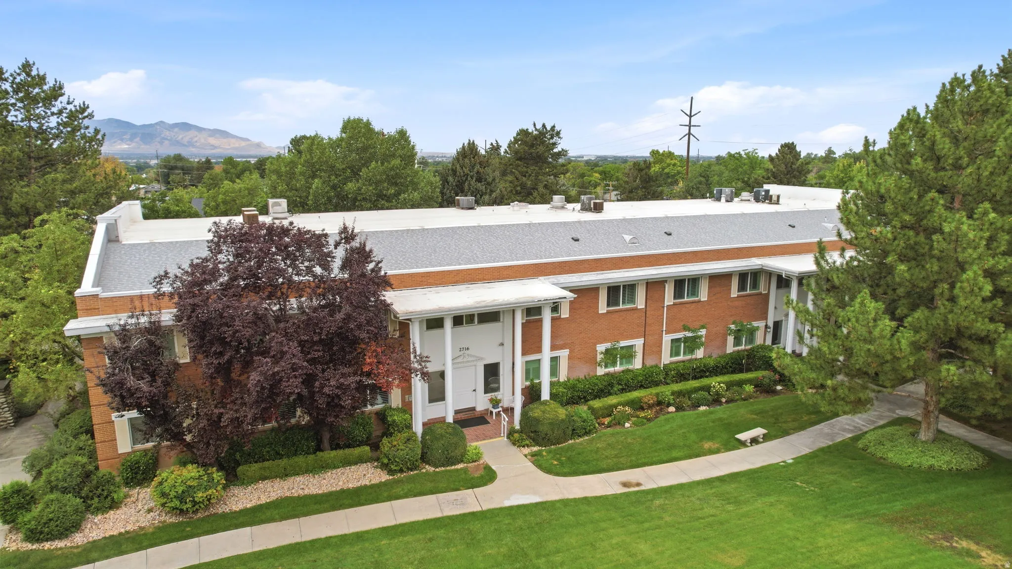 Brick exterior building with white columns and trim, featuring a meticulously maintained lawn, established landscaping, and a mountain backdrop