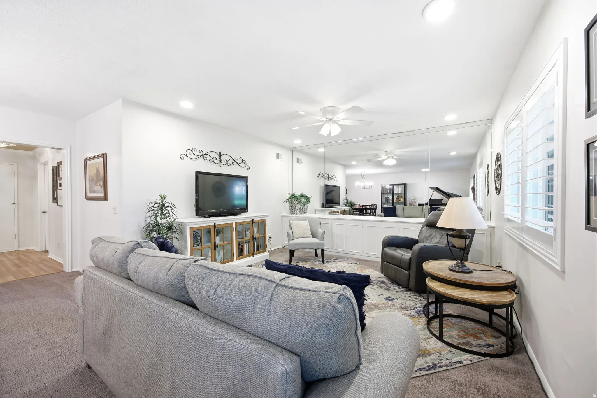 Recessed lighting illuminating the room, white plantation shutters, a ceiling fan, a full-length mirrored wall, and built-in white cabinetry