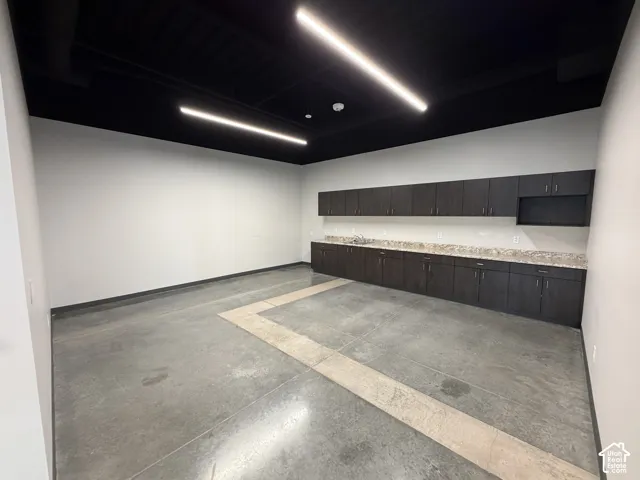 Polished concrete flooring, extensive dark wood-finish cabinetry, light-toned countertops, and contemporary linear ceiling lighting
