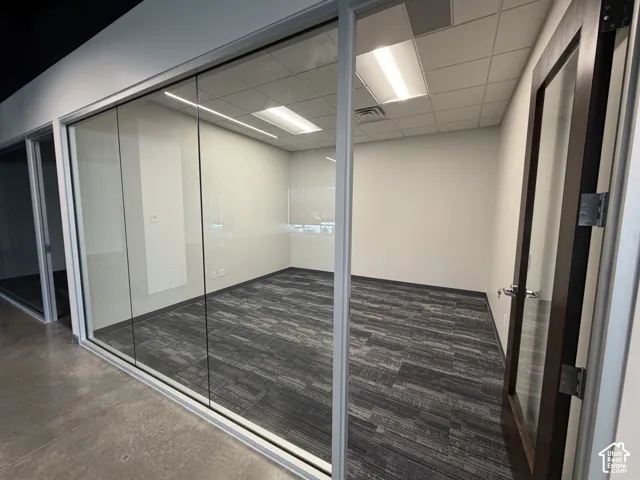 Glass partition walls with aluminum frames, patterned carpet flooring, recessed lighting, and a wood-finish door with glass inserts