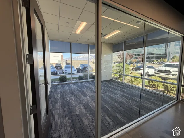 Floor-to-ceiling windows, patterned carpet flooring, recessed lighting, drop ceiling, and a full-light entry door