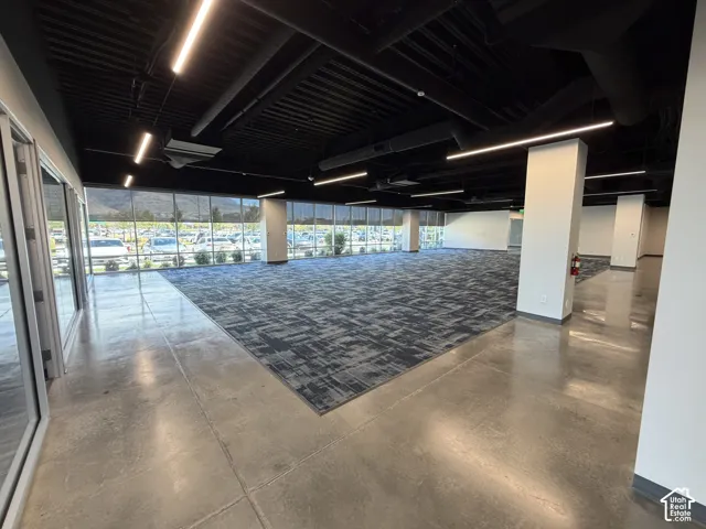 Expansive open-concept space featuring polished concrete flooring, patterned carpet, full-height windows, and linear ceiling lighting