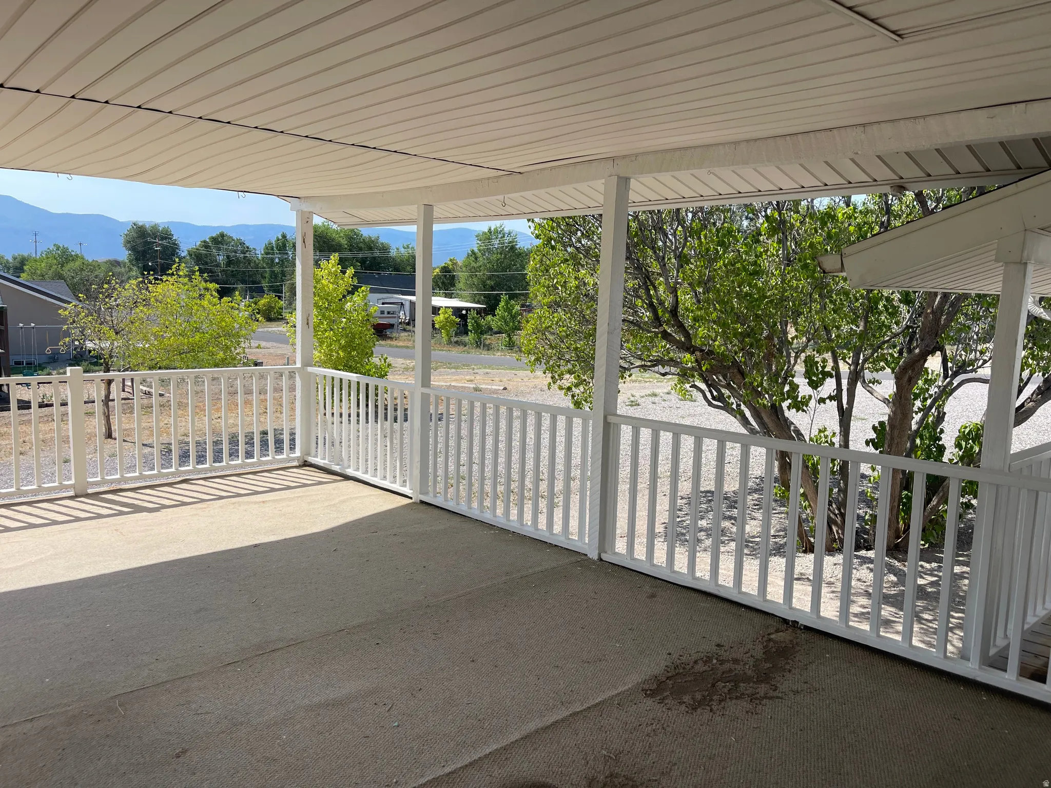 Covered patio featuring a concrete surface, white railing, and visible distant mountains