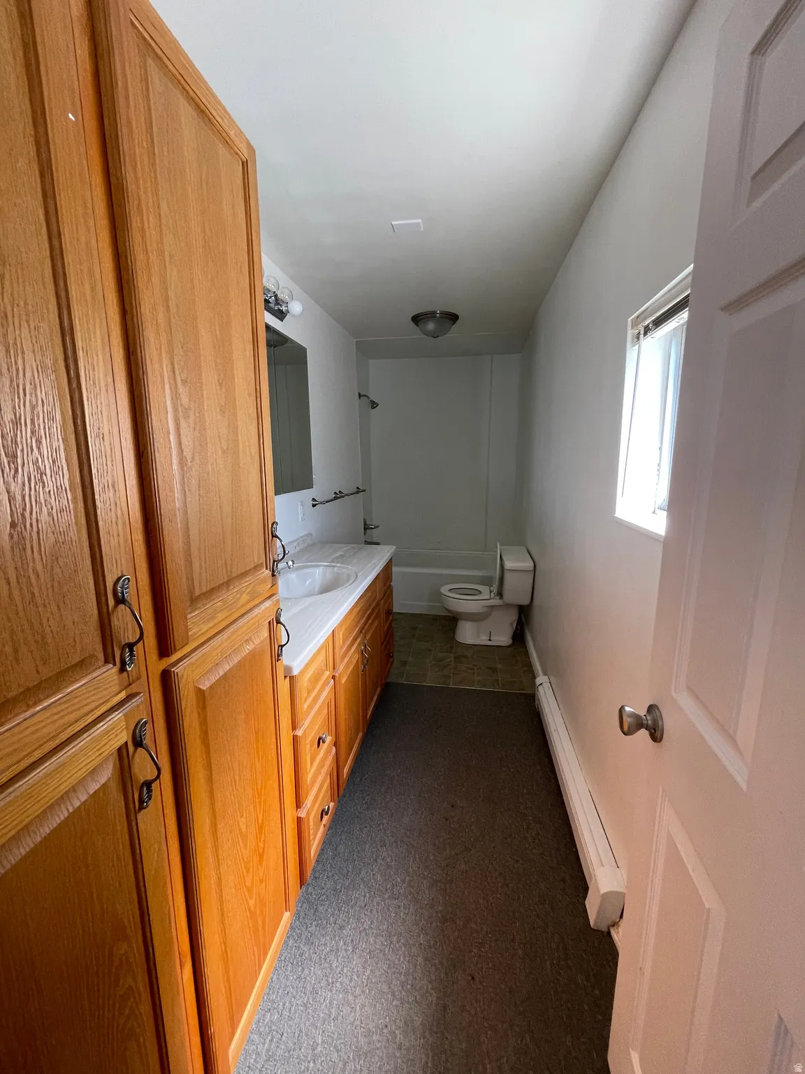Bathroom featuring a light wood-finish vanity with dual sinks, a matching built-in storage cabinet, and a white bathtub with shower
