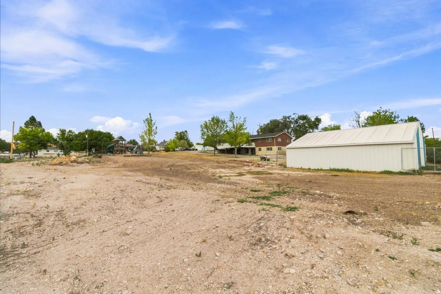 Expansive open lot featuring a large white metal outbuilding with a light-colored roof