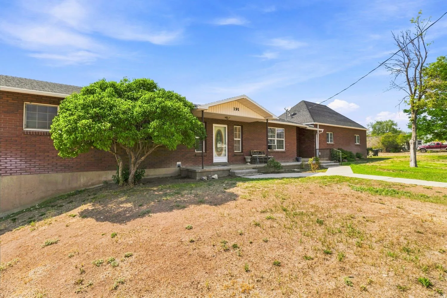 Brick exterior home with a covered front porch and mature tree