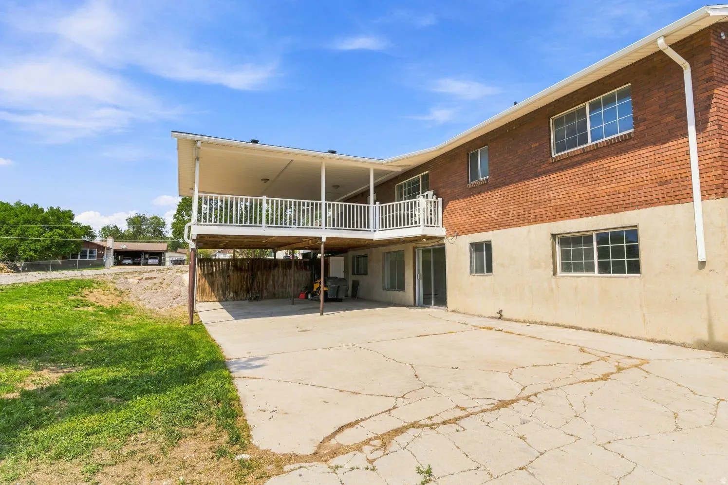 Rear exterior featuring a covered upper-level deck with white railings, a lower-level patio, and a grass lawn