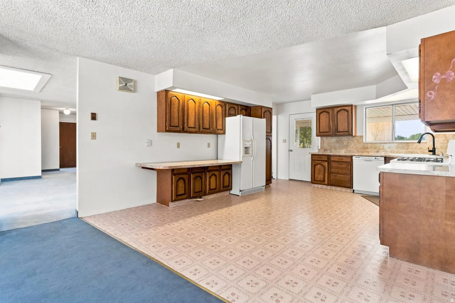 Kitchen featuring wood cabinetry, white appliances, patterned flooring, and a window above the sink