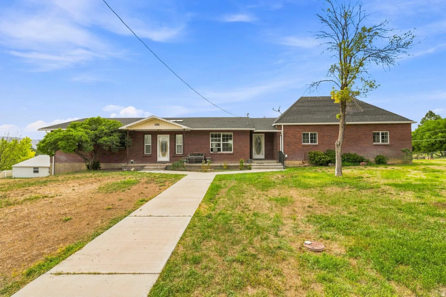 Brick exterior home with a light-colored porch entry, a concrete pathway, multiple windows, and a dark shingled roof