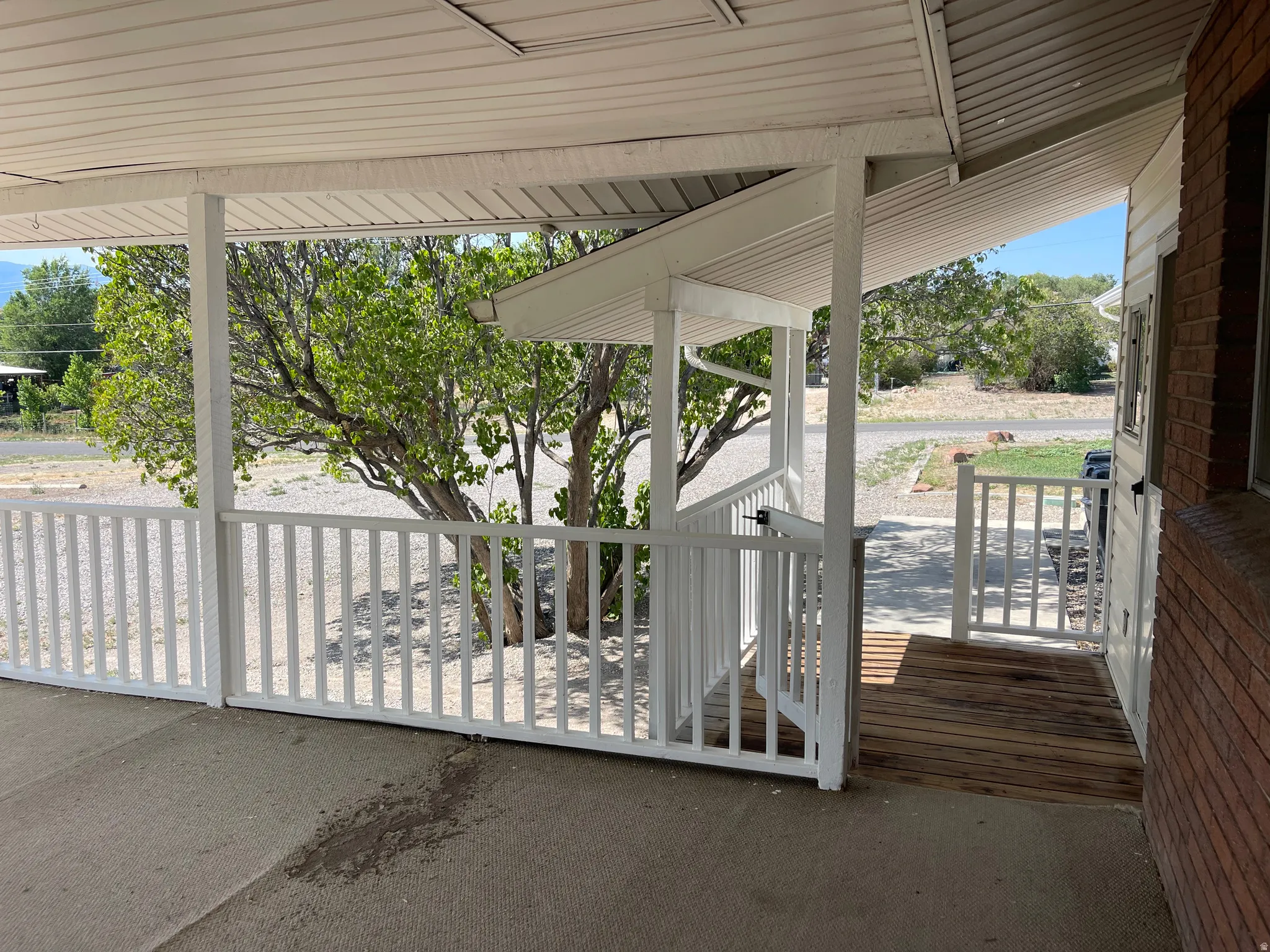 Covered porch featuring white railing, slatted wood ramp entry, and brick exterior siding
