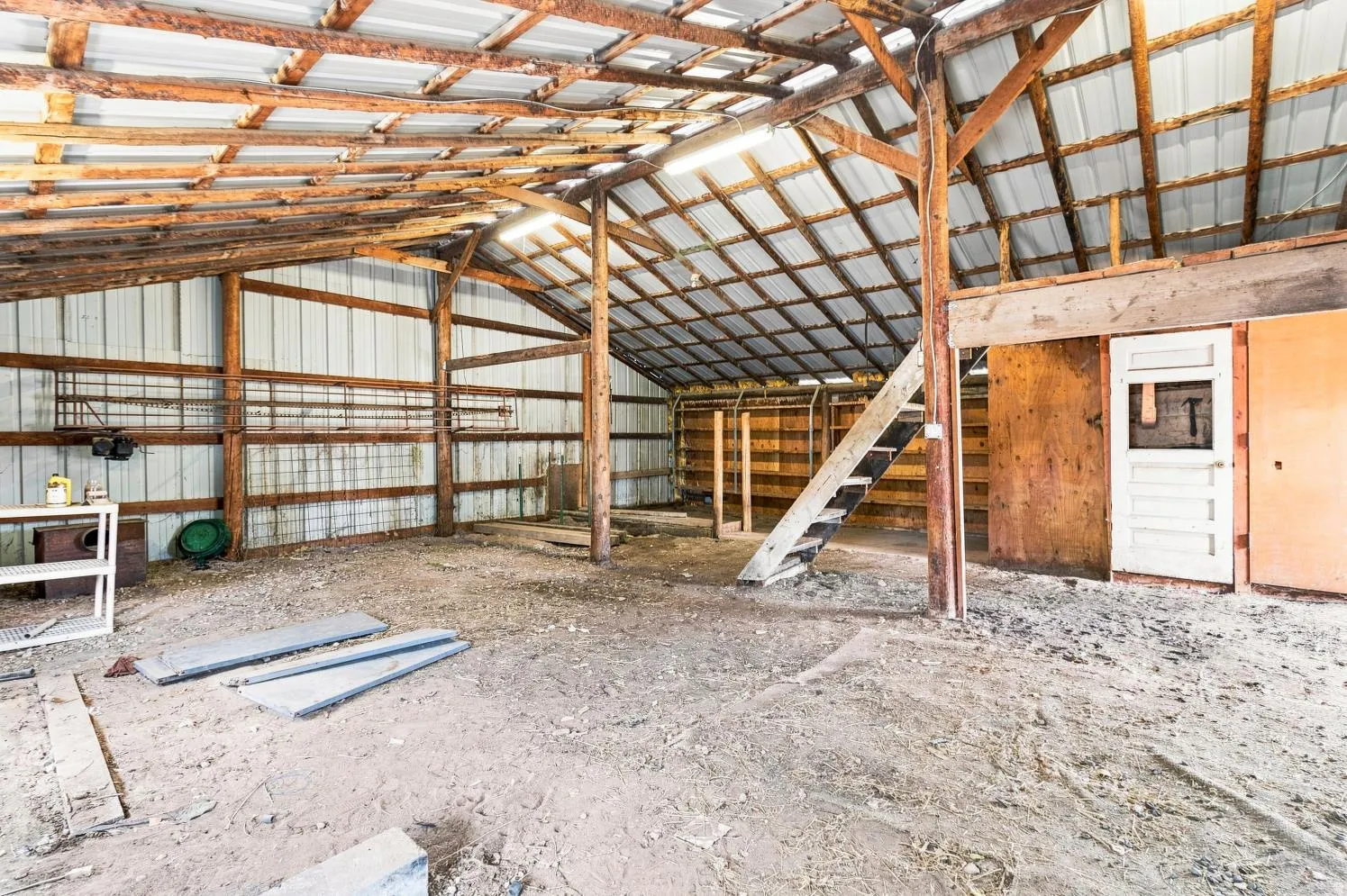 Interior barn space featuring exposed wood framing, corrugated metal walls and ceiling, a partial second-level loft, and an interior door