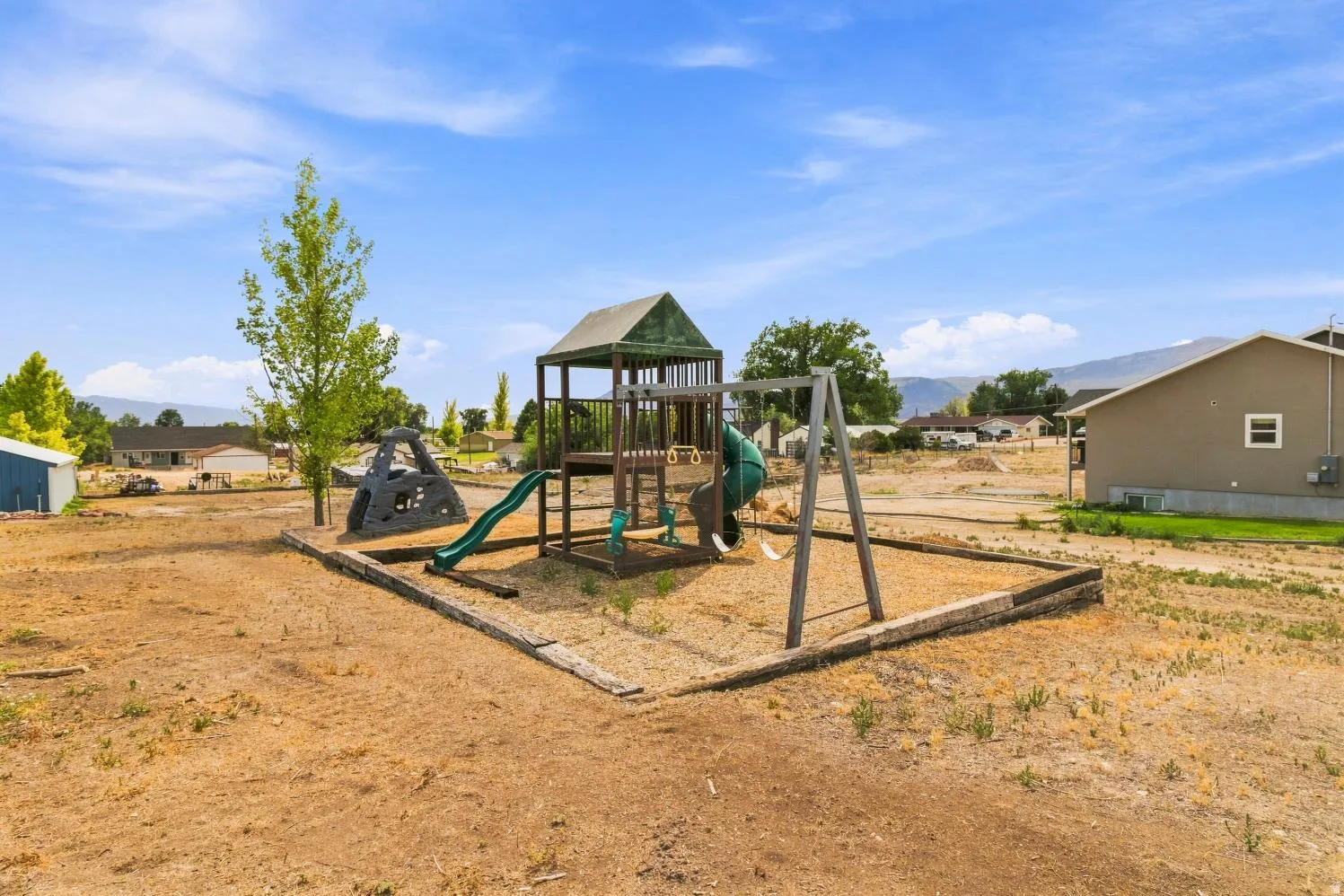 Outdoor play structure featuring a slide, swings, and climbing elements within a contained area