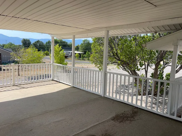 Covered patio featuring a concrete surface, white railing, and visible distant mountains