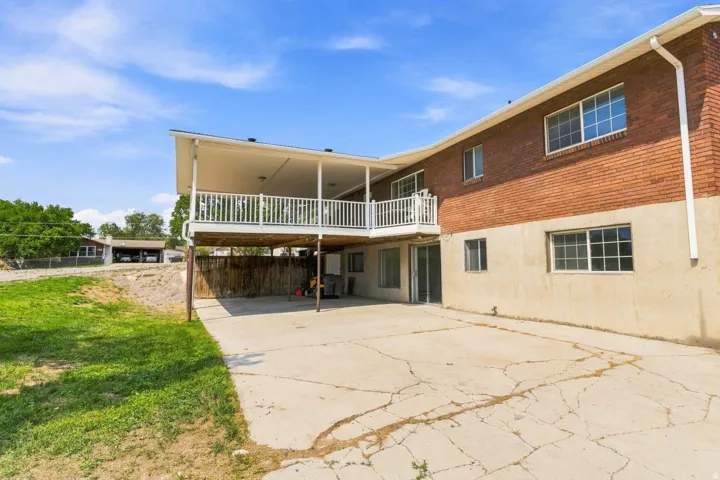Rear exterior featuring a covered upper-level deck with white railings, a lower-level patio, and a grass lawn