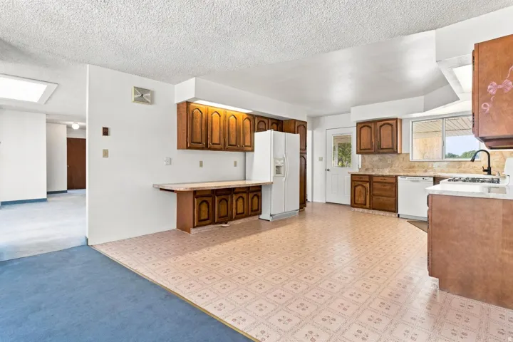 Kitchen featuring wood cabinetry, white appliances, patterned flooring, and a window above the sink