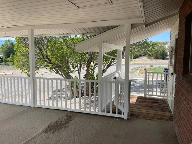 Covered porch featuring white railing, slatted wood ramp entry, and brick exterior siding