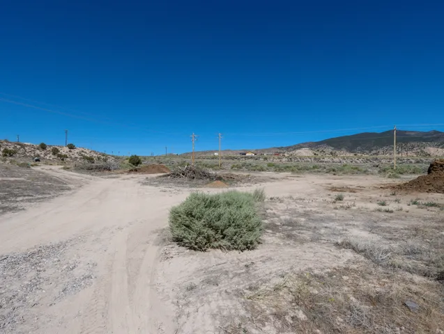 Expansive land parcel featuring a dirt path, natural vegetation, and distant mountain topography under a clear sky