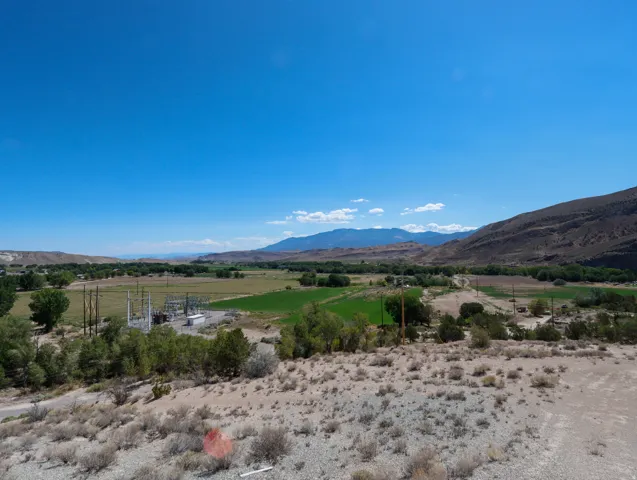 Expansive rural landscape featuring a valley with lush green fields, scattered trees, and surrounding mountains under a clear blue sky