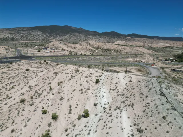 Expansive arid landscape featuring a clear blue sky, distant mountain range, and scattered low-lying vegetation