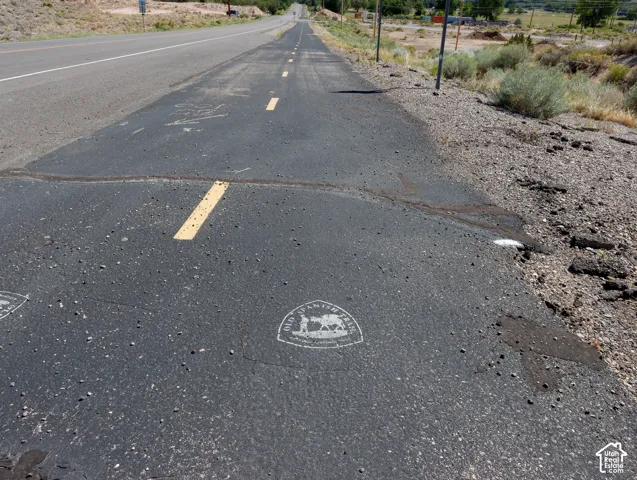 Paved road surface featuring a yellow dashed line, gravel shoulder, and a distant road extending into the landscape