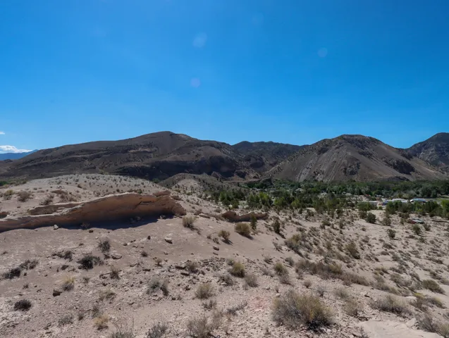 Expansive desert landscape featuring natural rock formations, scattered brush, and distant mountains