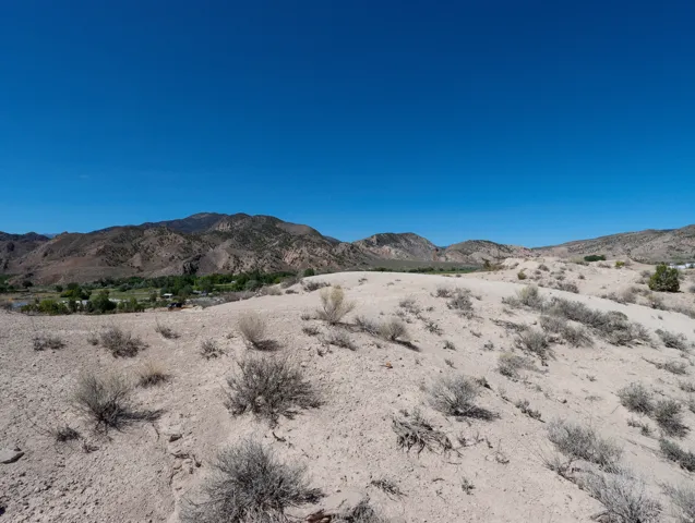 Expansive desert landscape featuring rugged terrain, scattered shrubbery, and distant mountains
