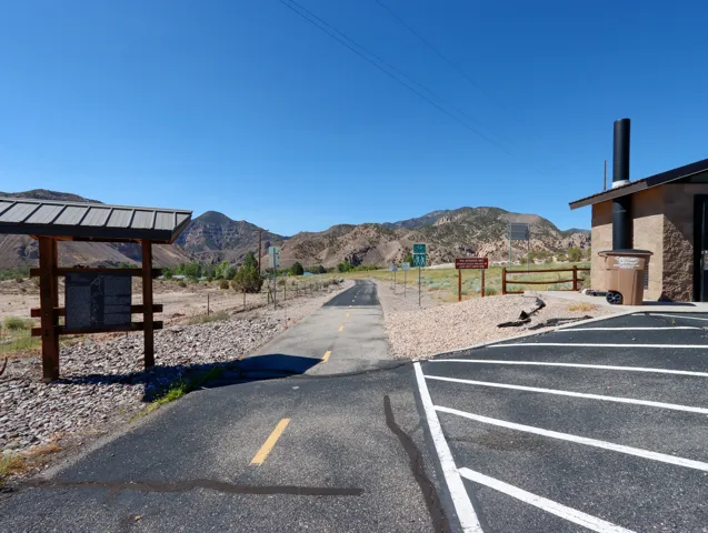 Asphalt parking area with painted lines, a paved path, and a stone-clad building