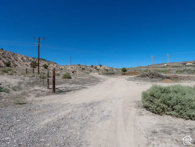 Expansive undeveloped land featuring a dirt road, partial fencing, arid vegetation, and utility poles