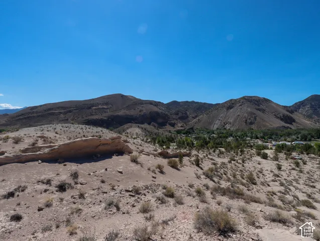 Expansive desert landscape featuring natural rock formations, scattered brush, and distant mountains