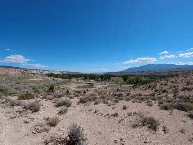 Expansive desert landscape featuring natural brush, distant mountains, and a clear blue sky