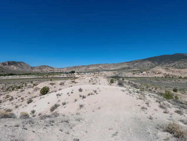 Expansive undeveloped land featuring rolling hills, sparse desert vegetation, distant mountains, and clear blue skies